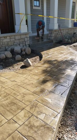 Close up of stamped concrete sidewalk to front step with man applying finishing touches