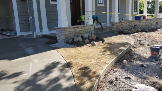 Curved driveway and transition to stamped concrete sidewalk to front porch of new model home.