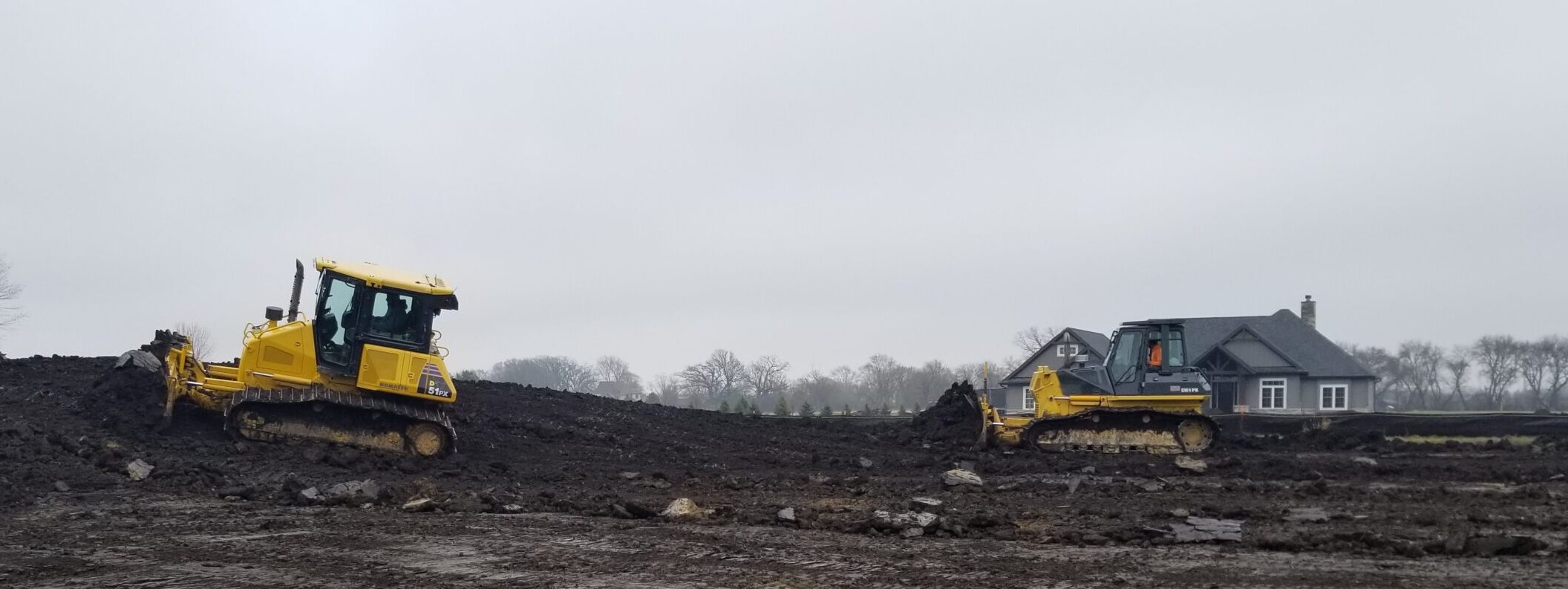 Two yellow bulldozers moving earth in preparation for a foundation.