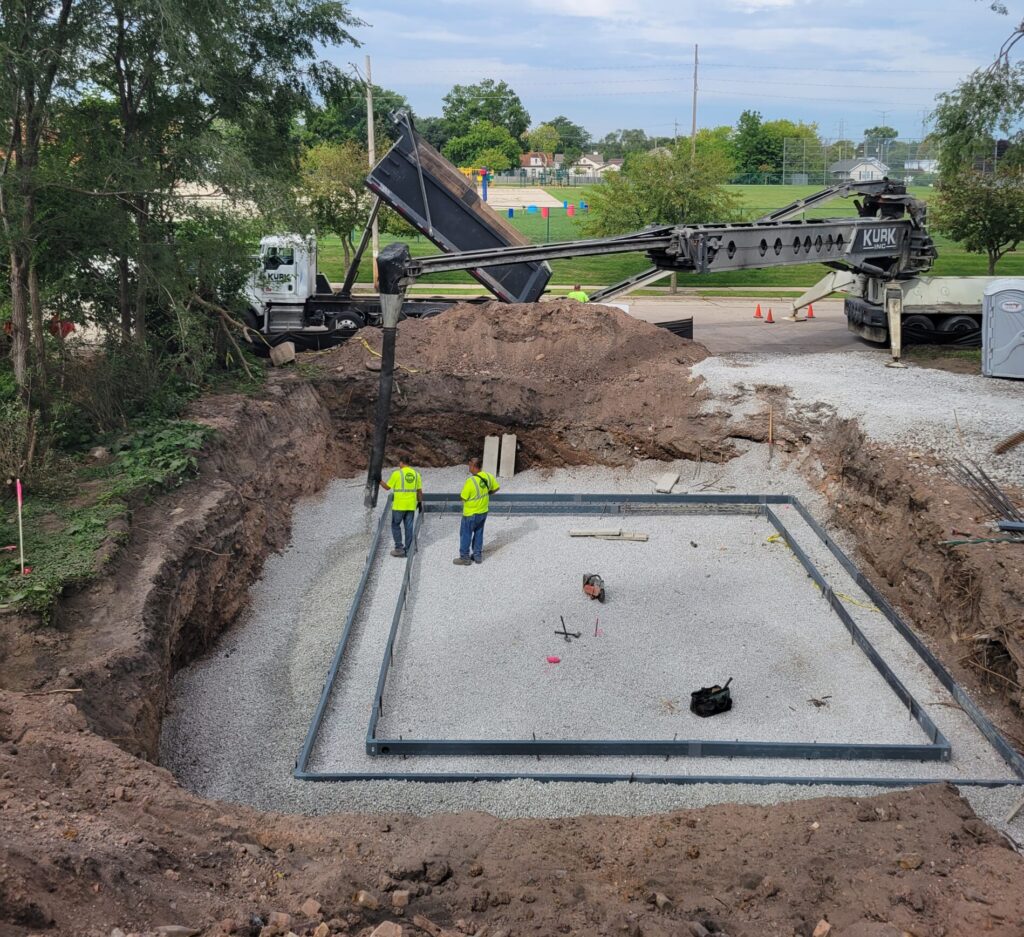 Two construction workers overseeing a foundation being filled in with rocks