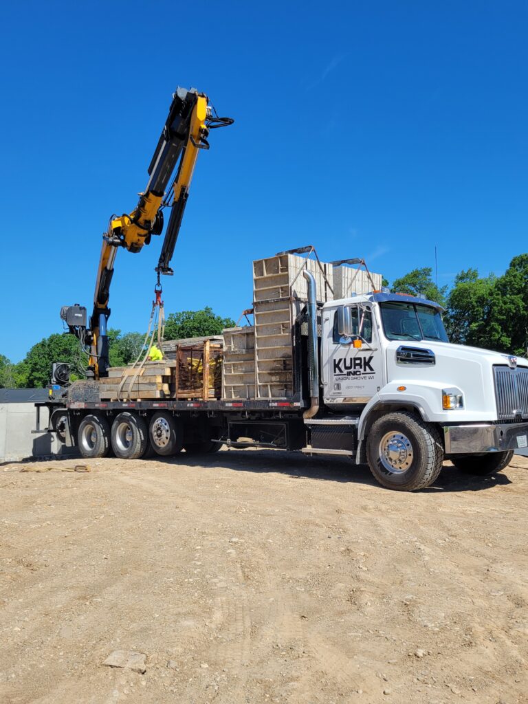 Kurk flatbed truck unloading concreete forms for a foundation.